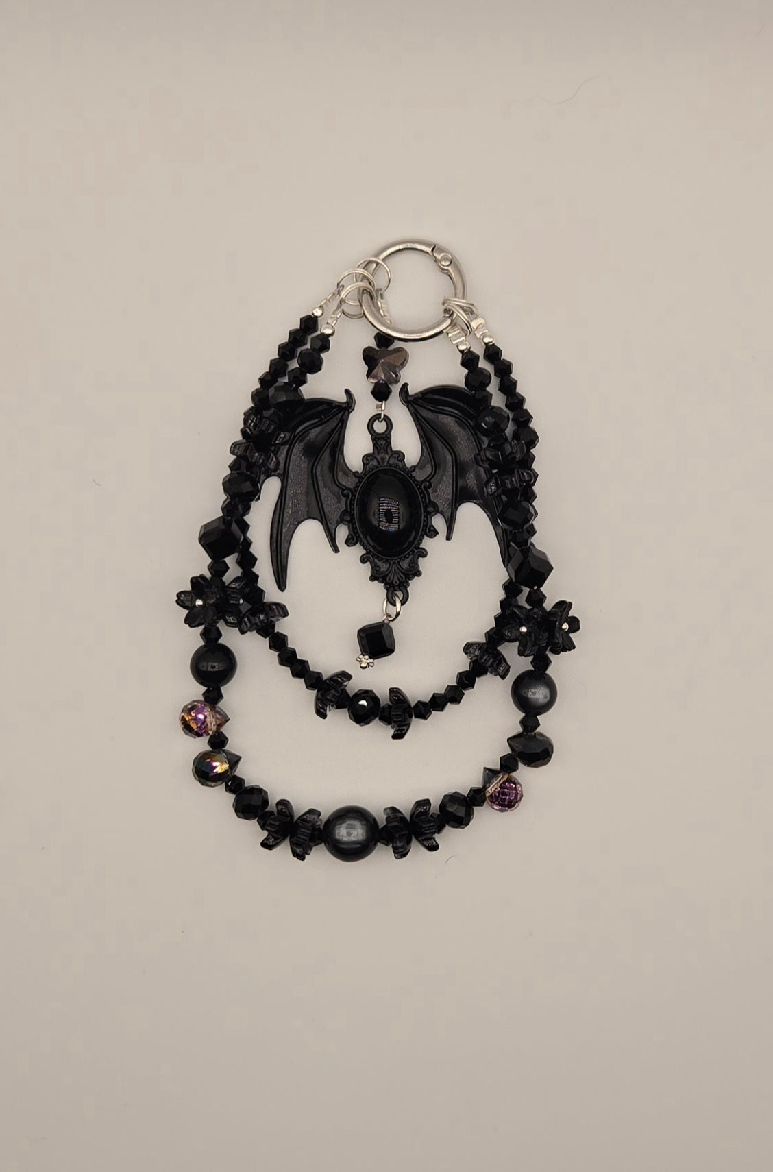 Black bat phone charm with ornate oval focal, layered black beads and floral accents