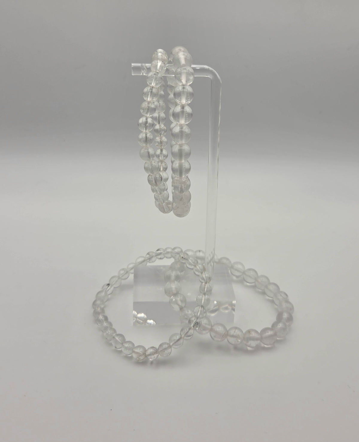 Acrylic stand: Clear quartz stretch bracelets with translucent round beads displayed on an acrylic jewelry stand