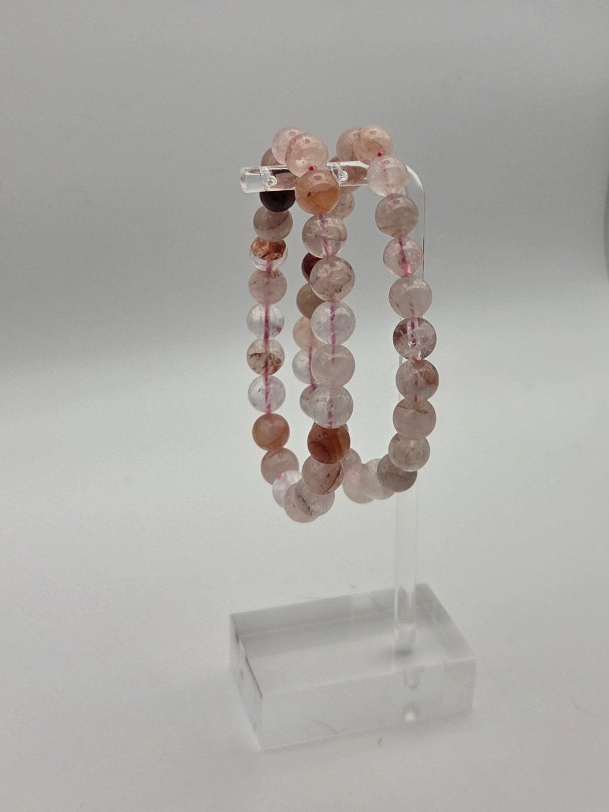 Acrylic stand: Fire quartz beaded stretch bracelets featuring blush pink peach and reddish brown stone beads on a clear acrylic stand
